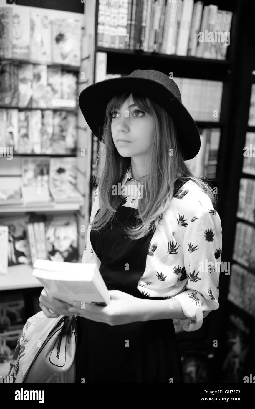 Fotografia di un 12 anni ragazza caucasion indossando un cappello nero in un comic book store azienda 2 Libri Manga Foto Stock