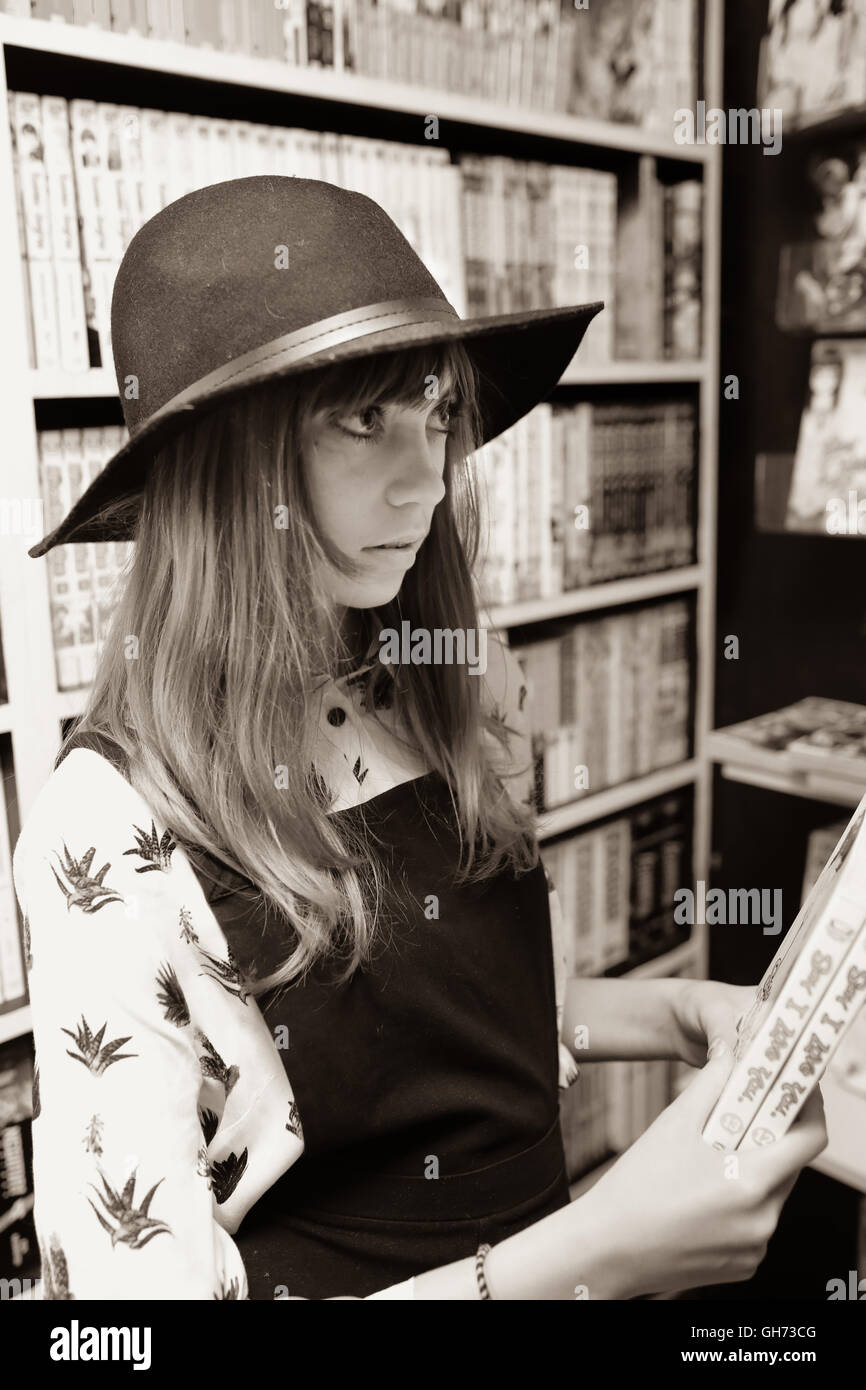 Seppia fotografia di un 12 anni ragazza indossando un cappello nero in un comic book store azienda 2 Libri Manga Foto Stock