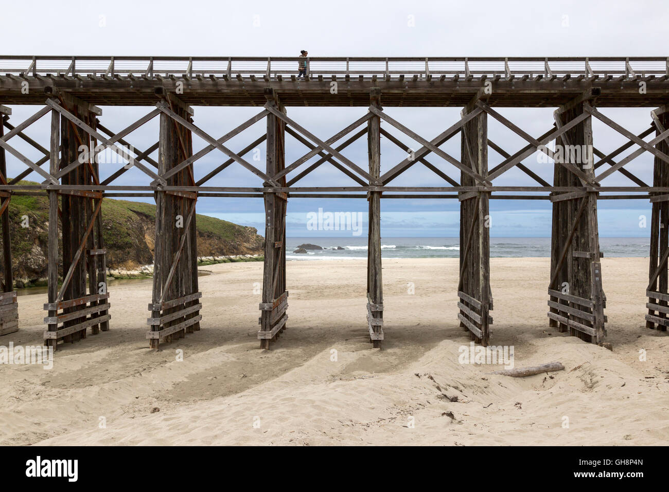 Vista laterale del lungo ponte di legno con vista oceano e giovane attraversando a piedi. Foto Stock