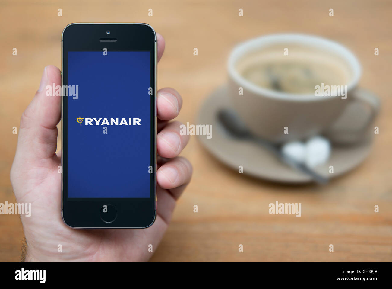 Un uomo guarda al suo iPhone che visualizza il logo di Ryanair, mentre sat con una tazza di caffè (solo uso editoriale). Foto Stock