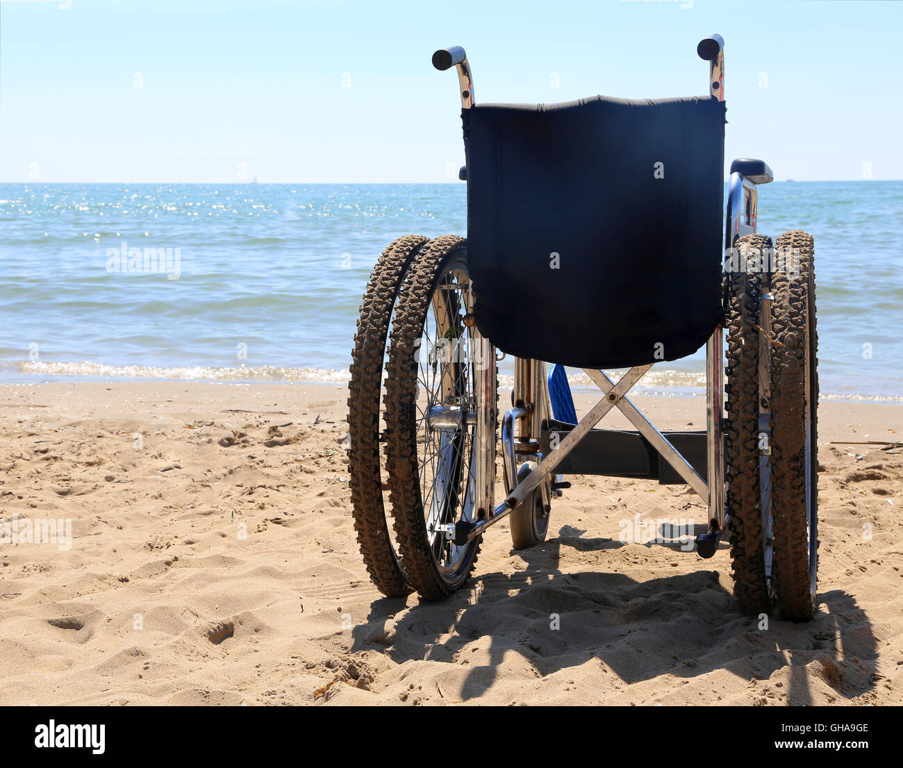 Grande sedia a rotelle sulla sabbia della spiaggia in estate Foto Stock