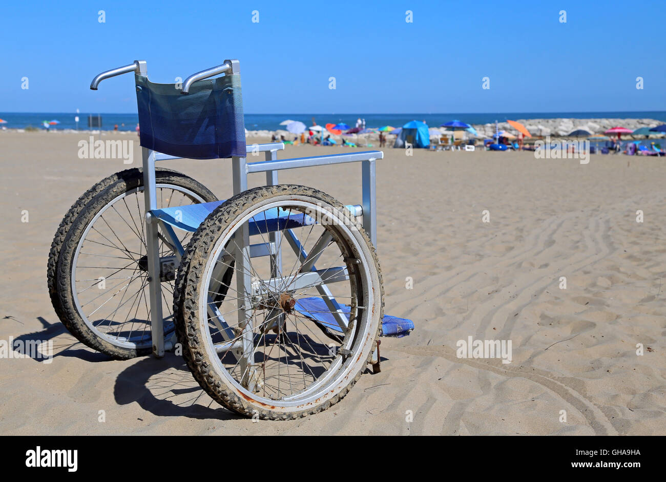 Sedia a rotelle di alluminio sulla sabbia e molti ombrelloni sulla spiaggia Foto Stock