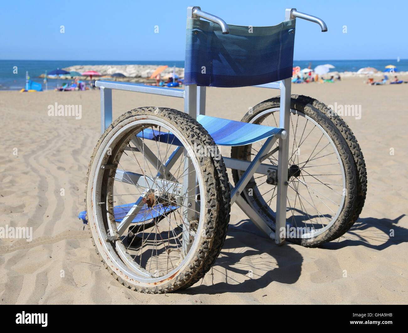 Sedia a rotelle sulla spiaggia di sabbia vicino al mare e molti ombrellino in background Foto Stock