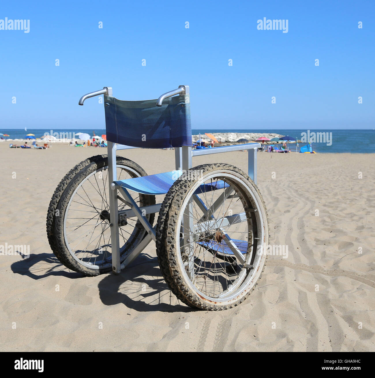 Sedia a rotelle moderno sulla spiaggia di sabbia vicino al mare con molti ombrelloni Foto Stock