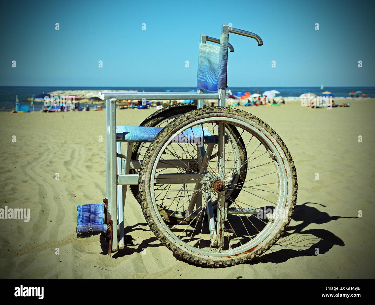 Sedia a rotelle sulla spiaggia di sabbia vicino al mare con ombrelloni Foto Stock