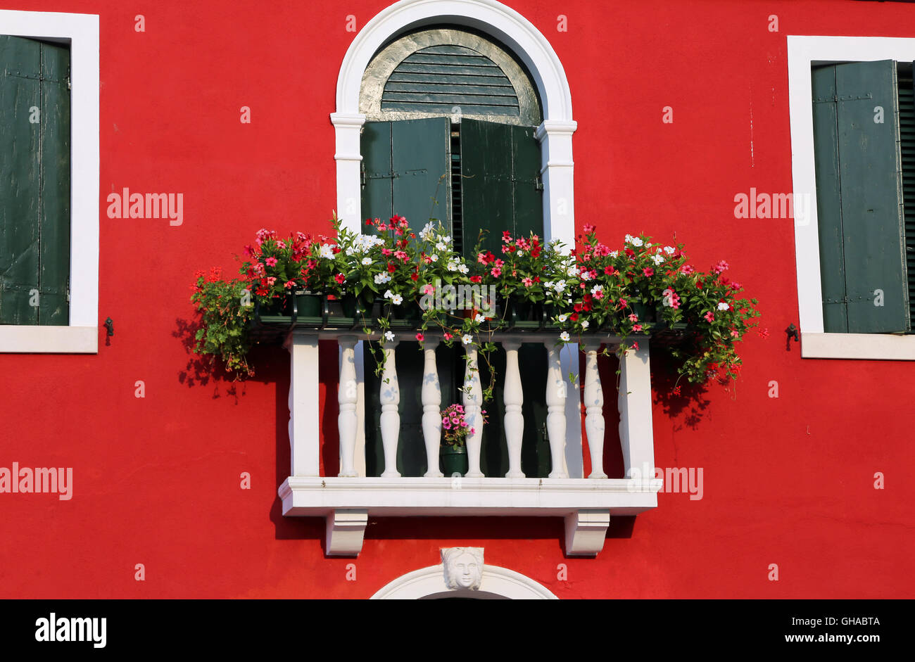 Bellissimo balcone fiorito con una finestra in casa e molti vasi di fiori Foto Stock