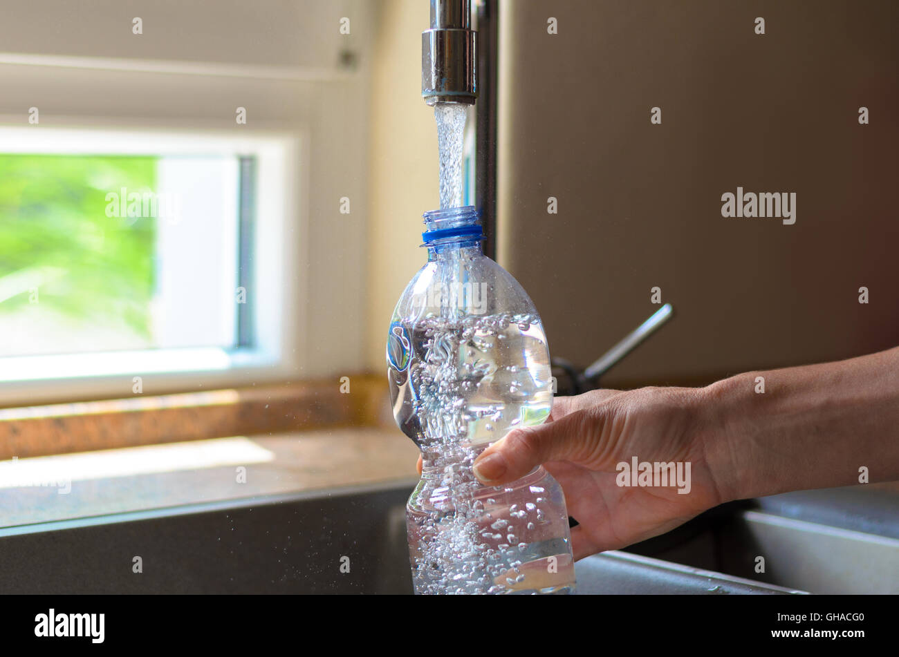 Donna di riempimento di una bottiglia di plastica con acqua di rubinetto in cucina con una vista ravvicinata in acqua corrente, bolle di aria Foto Stock