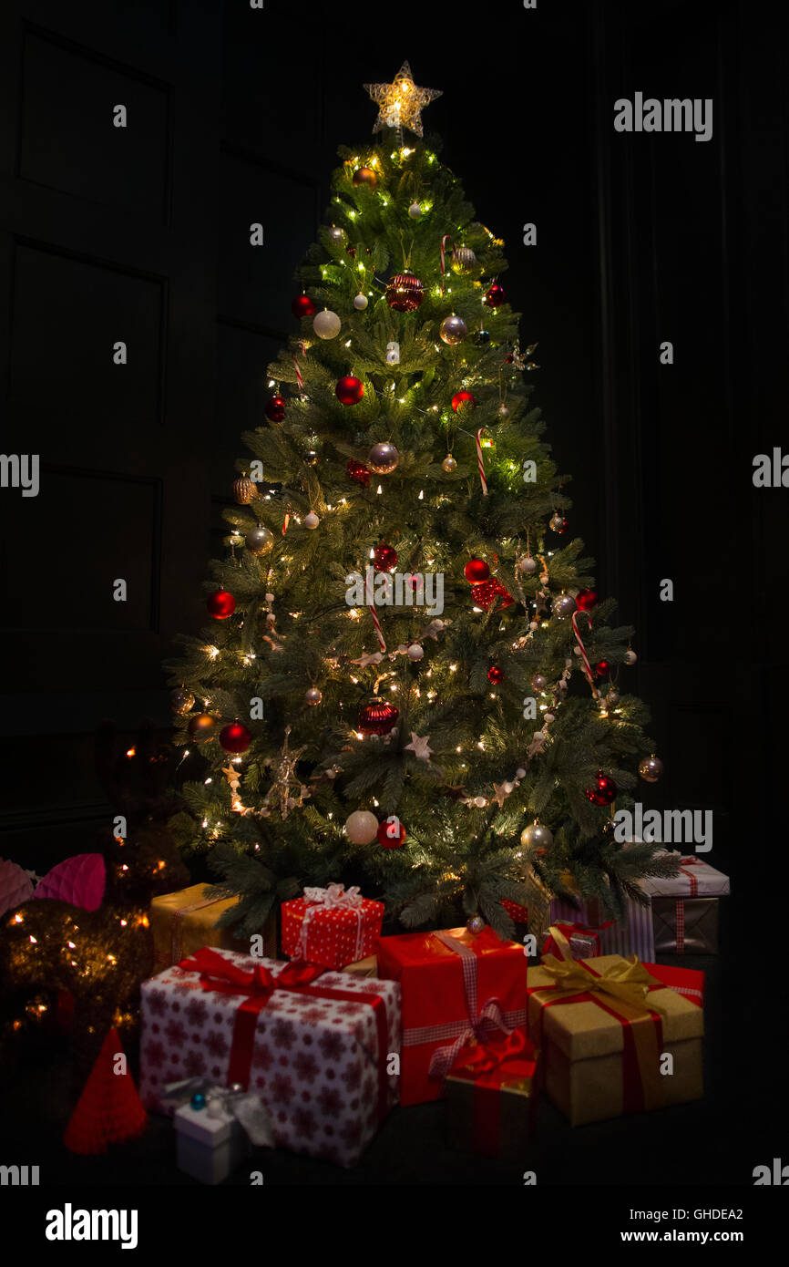 Illuminato albero di Natale circondato da omaggi in camera oscura Foto Stock
