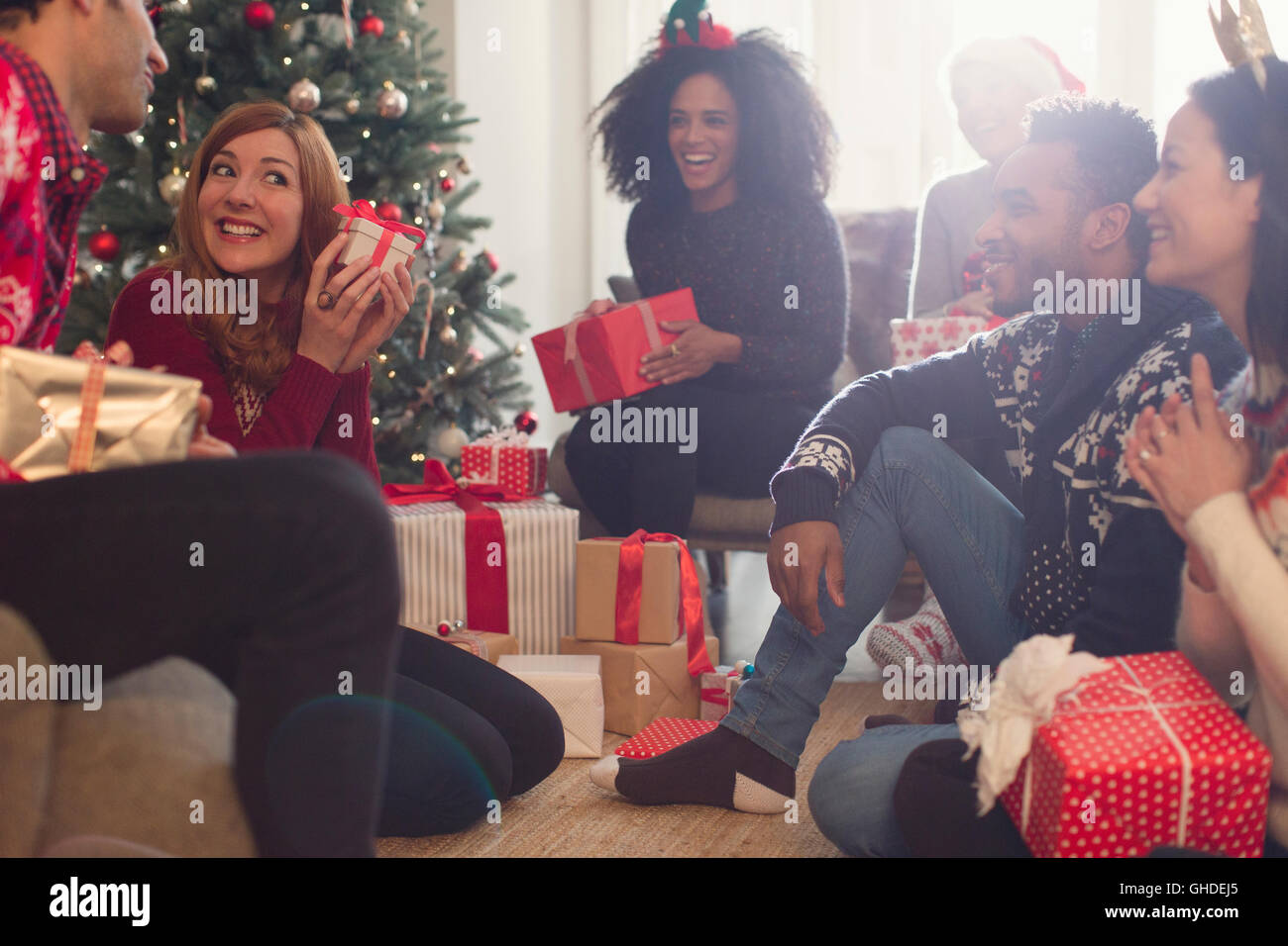 Gli amici a guardare giocosa donna scuotendo regalo di Natale Foto Stock