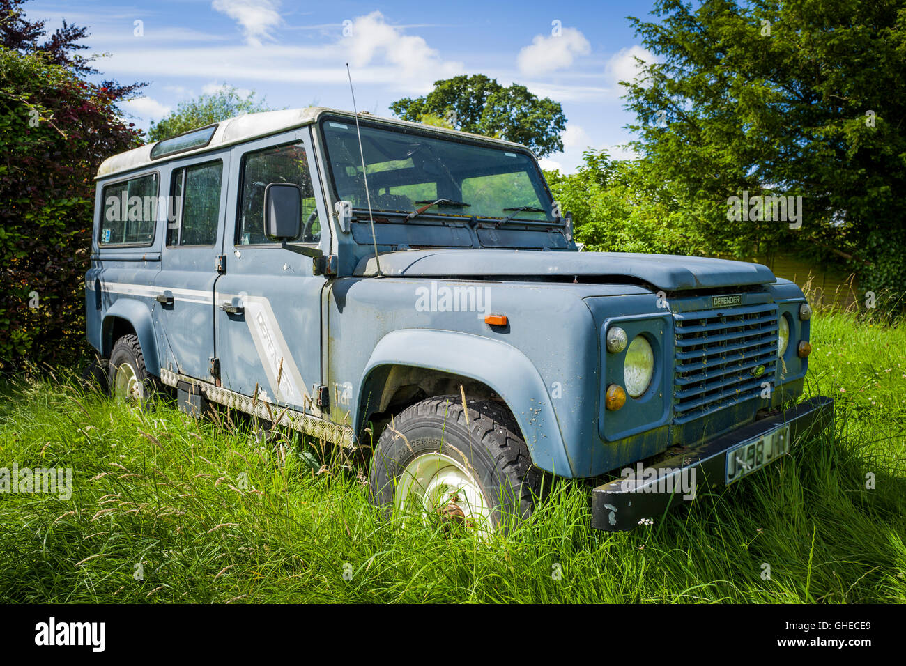 Il vecchio Land Rover Defender ritirato in erba lunga in attesa di restauro Foto Stock