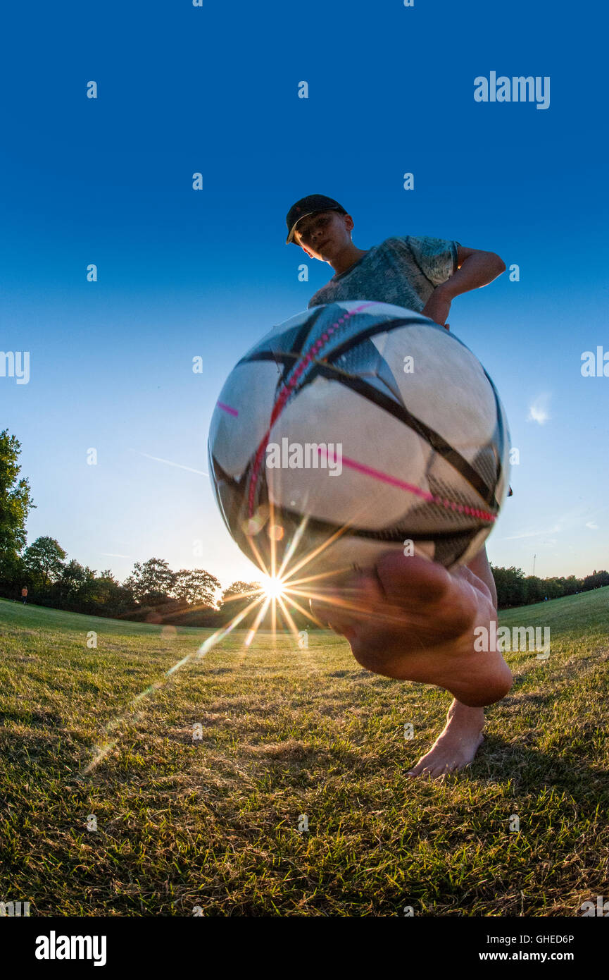 Un ragazzo giocando a calcio, eseguire trucchi improvvisati in un parco urbano a giocare Foto Stock