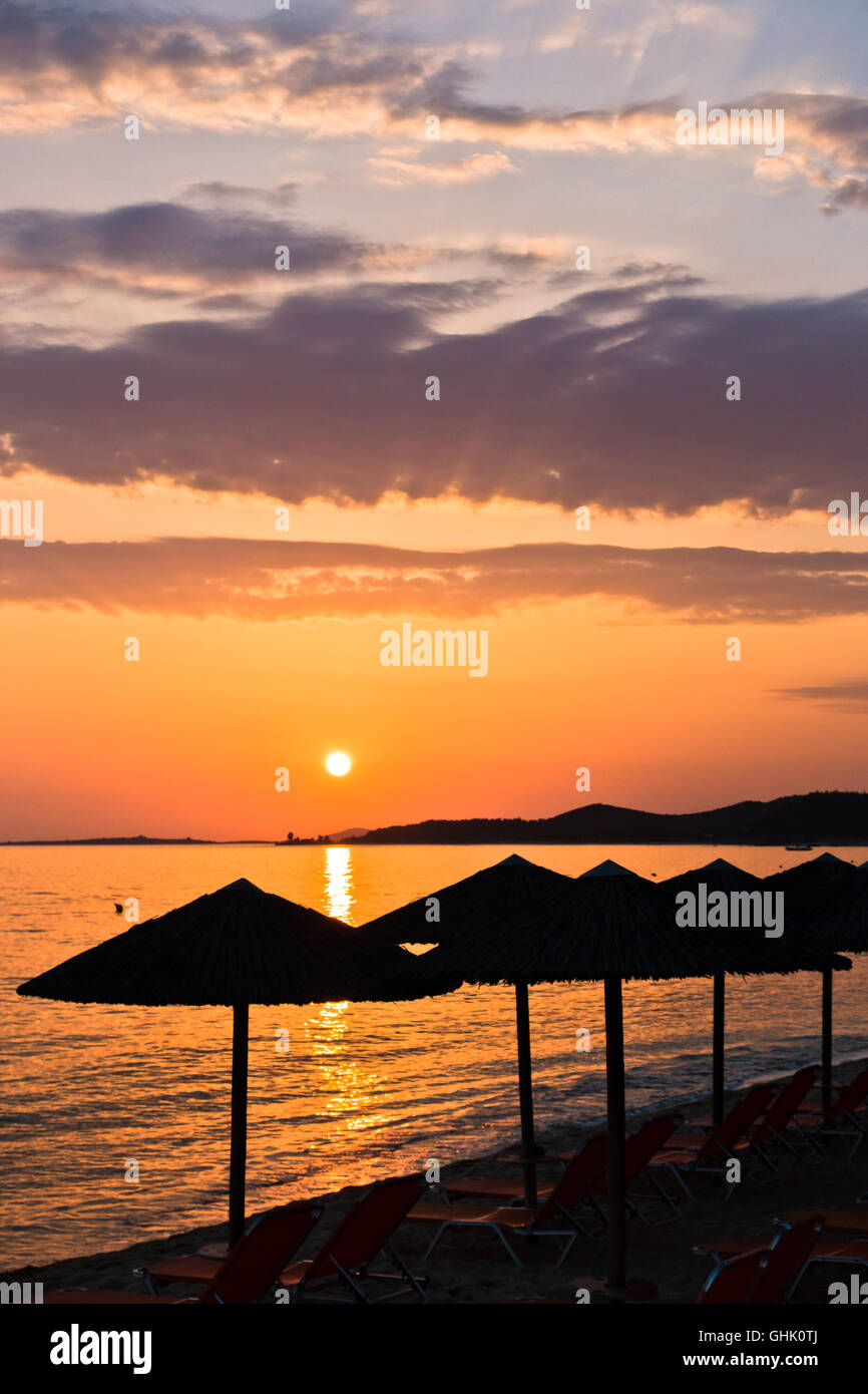 Spiaggia di sabbia con stray ombrelloni e sedie di colore arancione al tramonto in Sithonia Foto Stock