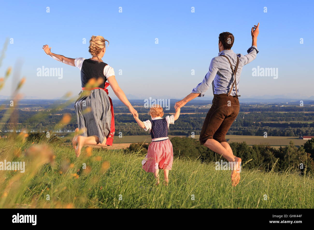 Una famiglia tedesca in abito bavarese jumping happy prato Foto Stock