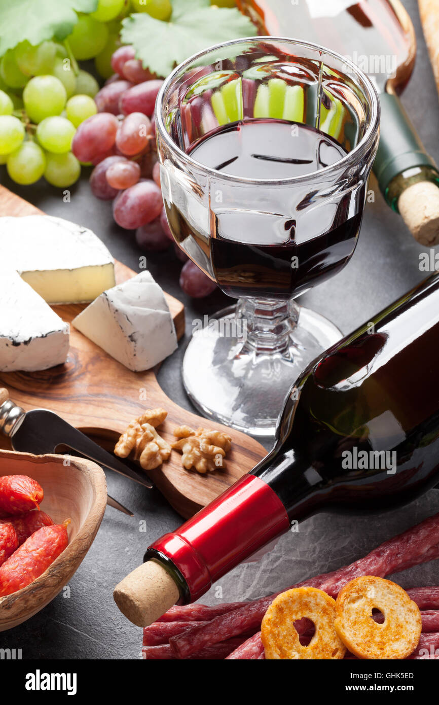 Vino rosso e bianco, uva, formaggio e salsicce su tavolo di pietra Foto Stock