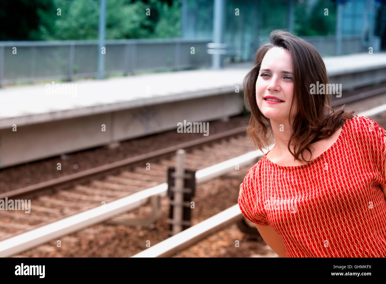 Giovane donna in abito rosso in attesa alla stazione ferroviaria Foto Stock