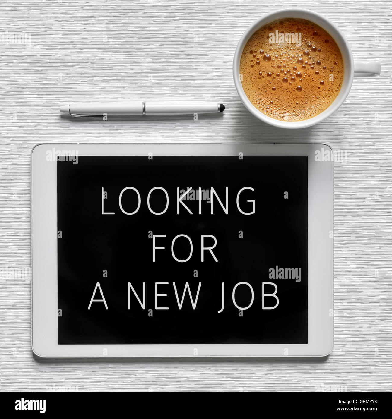 Alta angolazione di un computer tablet con il testo in cerca di un nuovo posto di lavoro nel suo schermo, una tazza di caffè e una penna digitale su un w Foto Stock