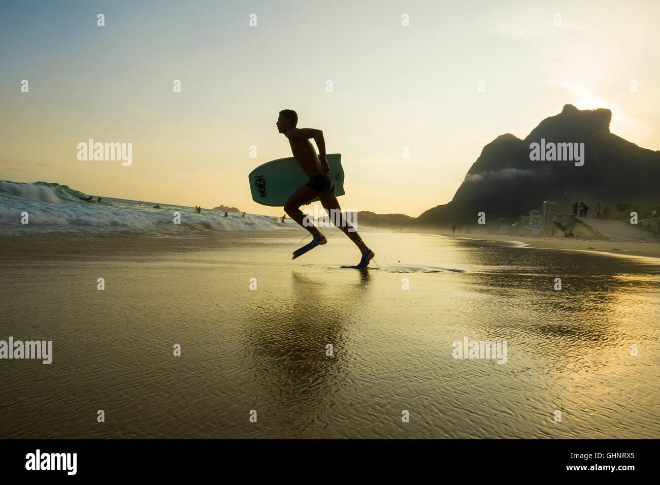 RIO DE JANEIRO - Marzo 8, 2016: Bodyboarder corre tra le onde su São Conrado spiaggia sotto una silhouette al tramonto. Foto Stock