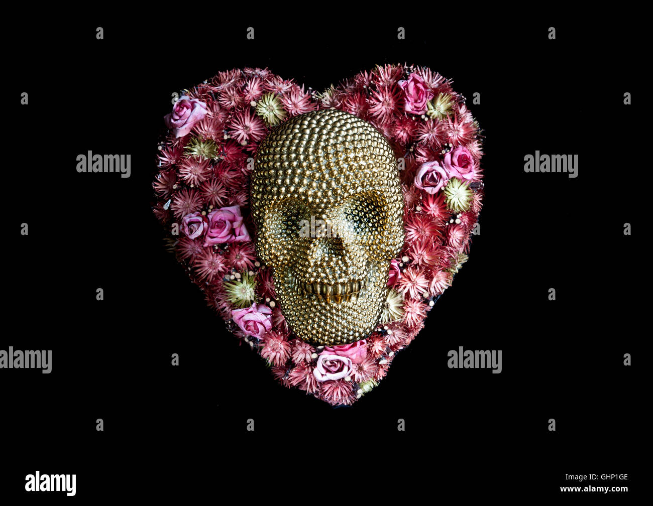 Concetto di immagine di sorridere oro cranio giacente sul fiore a forma di cuore la disposizione su sfondo nero Foto Stock