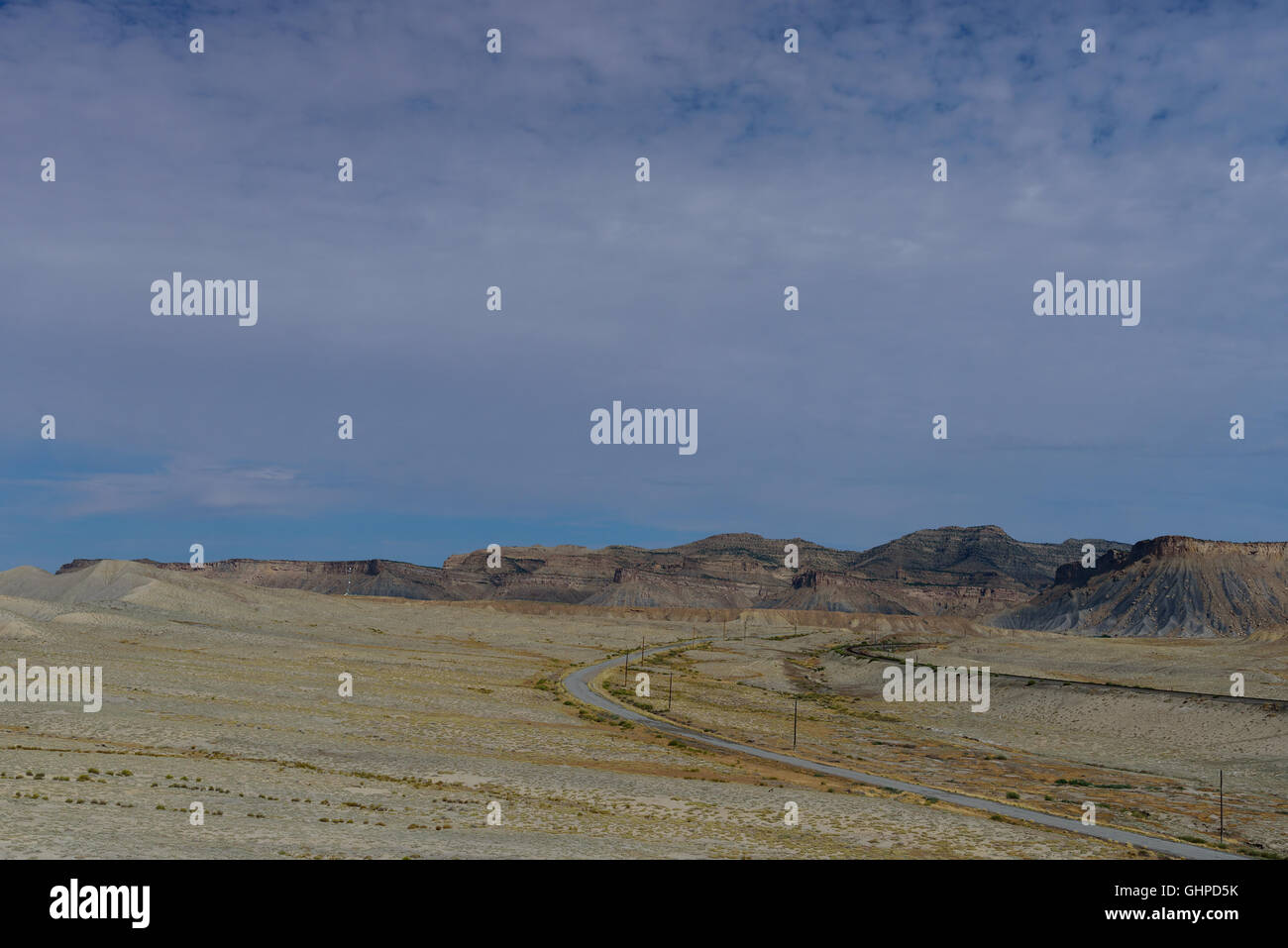 Strada solitaria della curvatura attraverso il deserto piano terreno sotto il cielo blu. Utah, Stati Uniti d'America Foto Stock