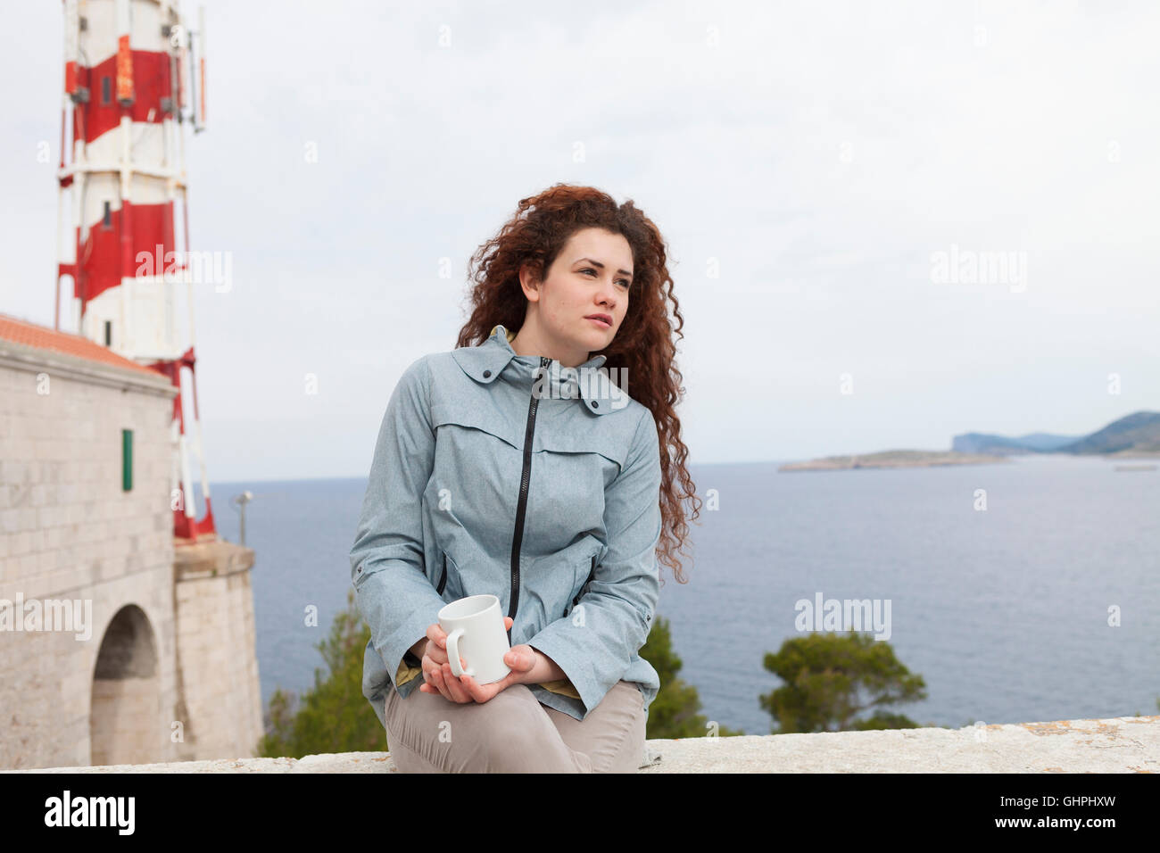 Giovane donna si prende una pausa con il faro in background Foto Stock