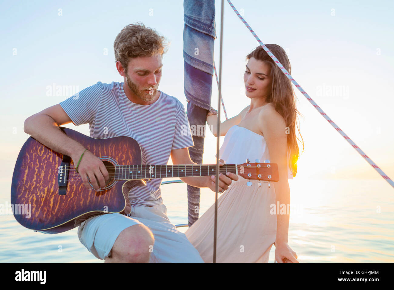 Giovane uomo a suonare la chitarra in barca a vela Foto Stock
