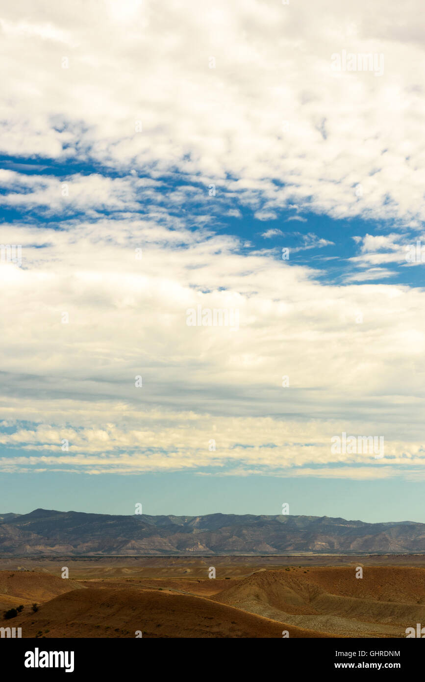 Arido utah, usa marrone colline con montagne rocciose nella distanza sotto il cielo blu con nuvole bianche. immagine verticale. Foto Stock