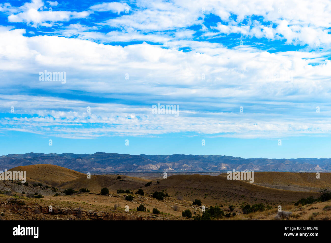 Marrone colline sotto il cielo blu con nuvole bianche, montagne in distanza. Foto Stock