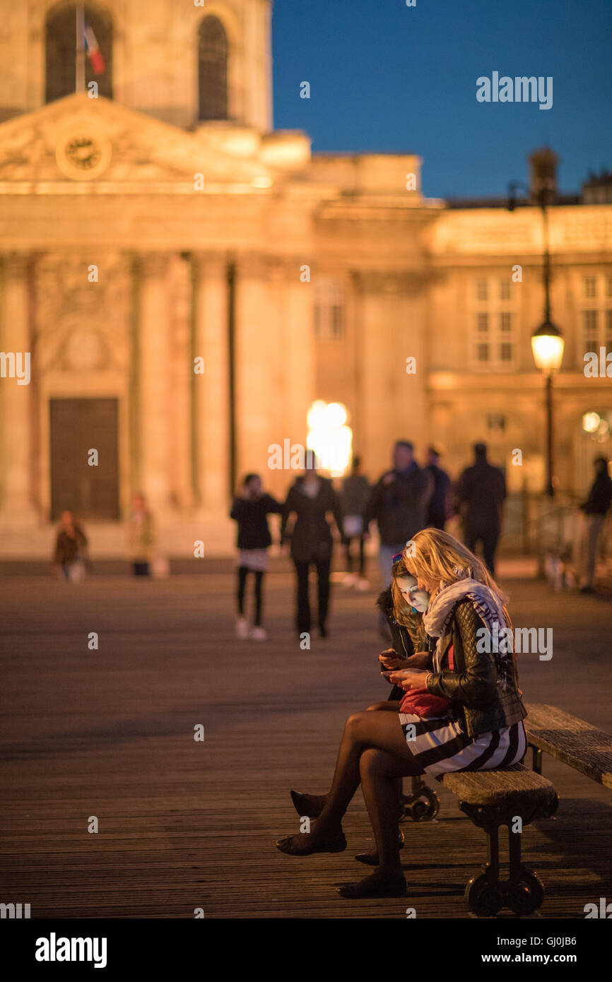 Due donne sui loro telefoni cellulari sul Pont des Arts al crepuscolo, Parigi, Francia Foto Stock