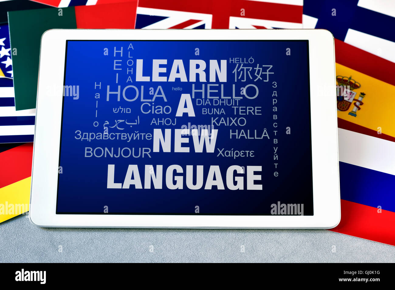 Il testo imparare una nuova lingua e la parola hello in diverse lingue sullo schermo di un computer tablet, circondato da bandiere Foto Stock
