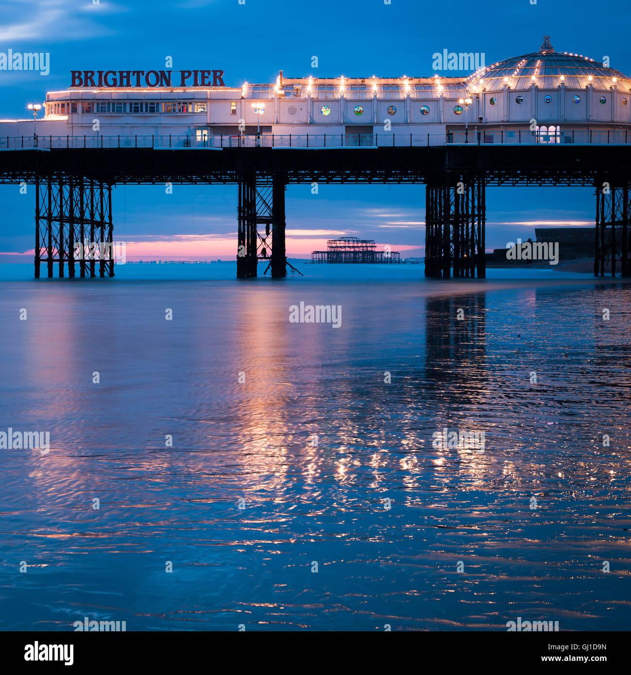 Il Brighton Pier al tramonto si riflette nella sabbia bagnata della bassa marea. In lontananza il vecchio molo Ovest può essere visto. Foto Stock