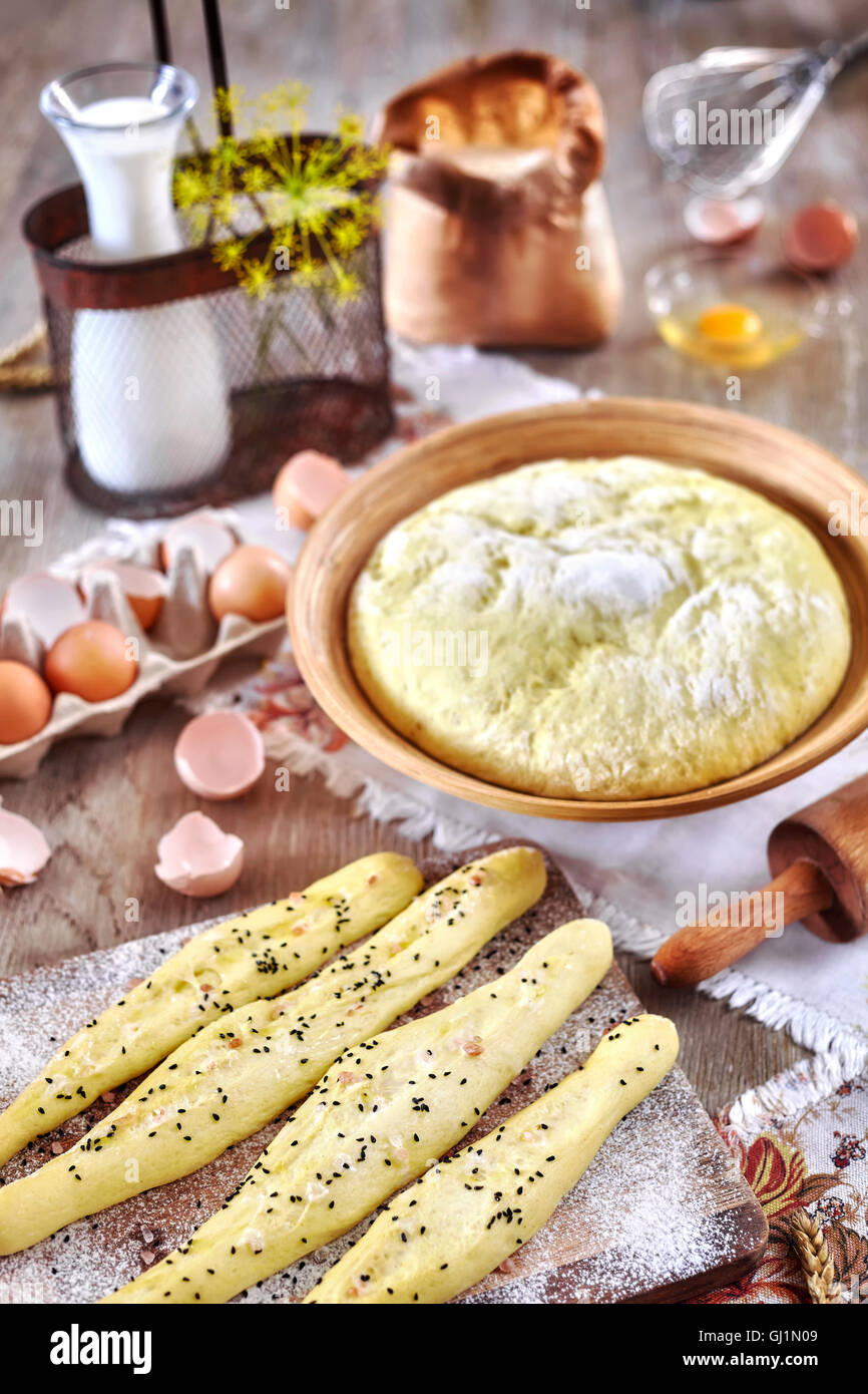 Bastoncini di pane e pasta lievitata pronti per la cottura, locale rustico su un tavolo di legno. Foto Stock