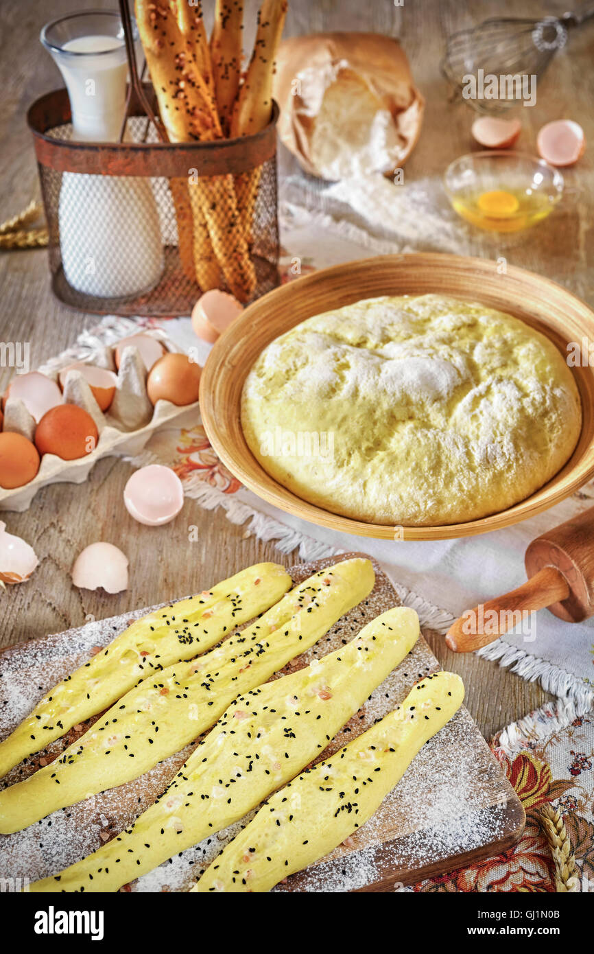 Bastoncini di pane e pasta lievitata pronti per la cottura, locale rustico su un tavolo di legno. Foto Stock