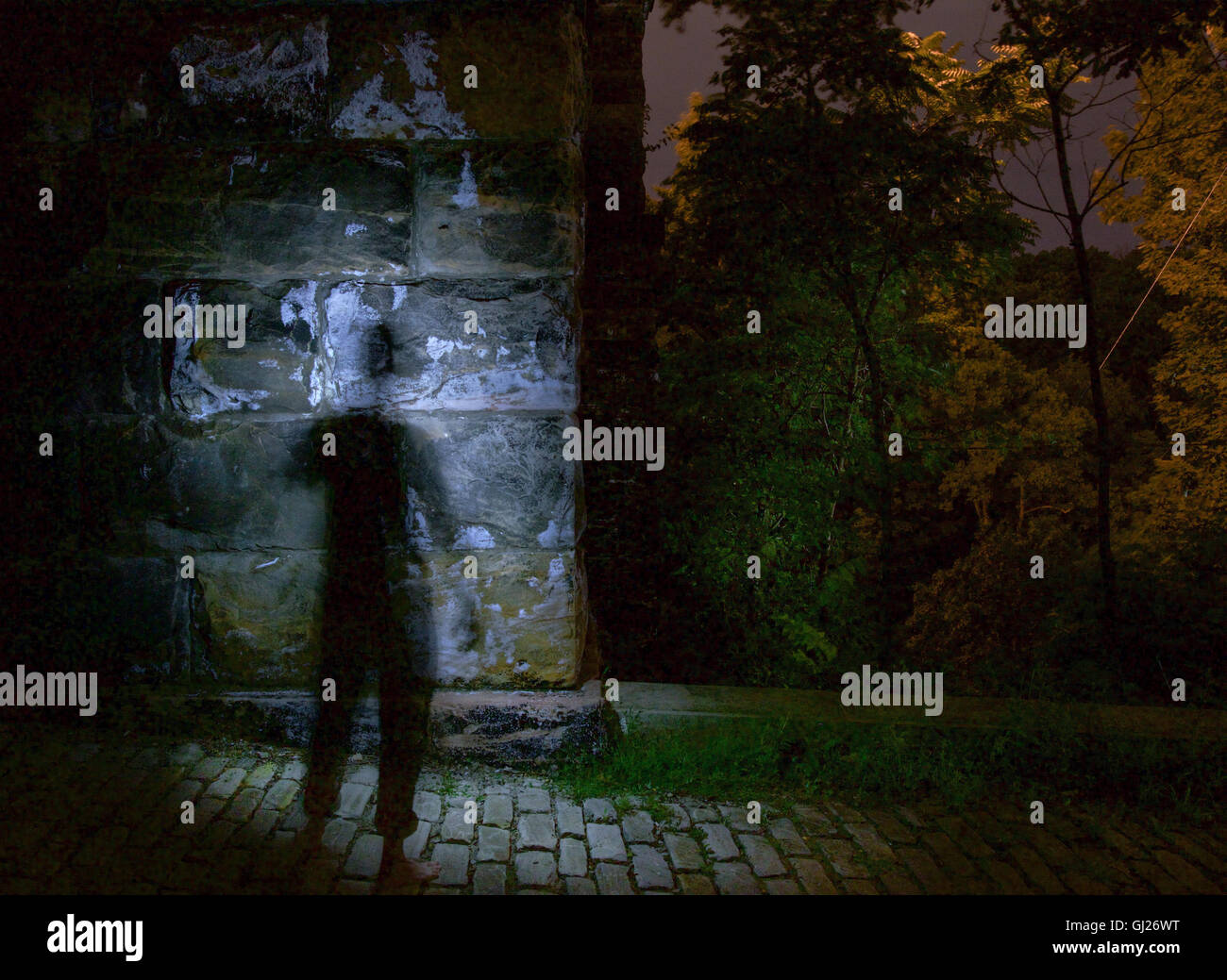 Figura oscura accanto a una pietra illuminato pilastro sotto un ponte di notte Foto Stock