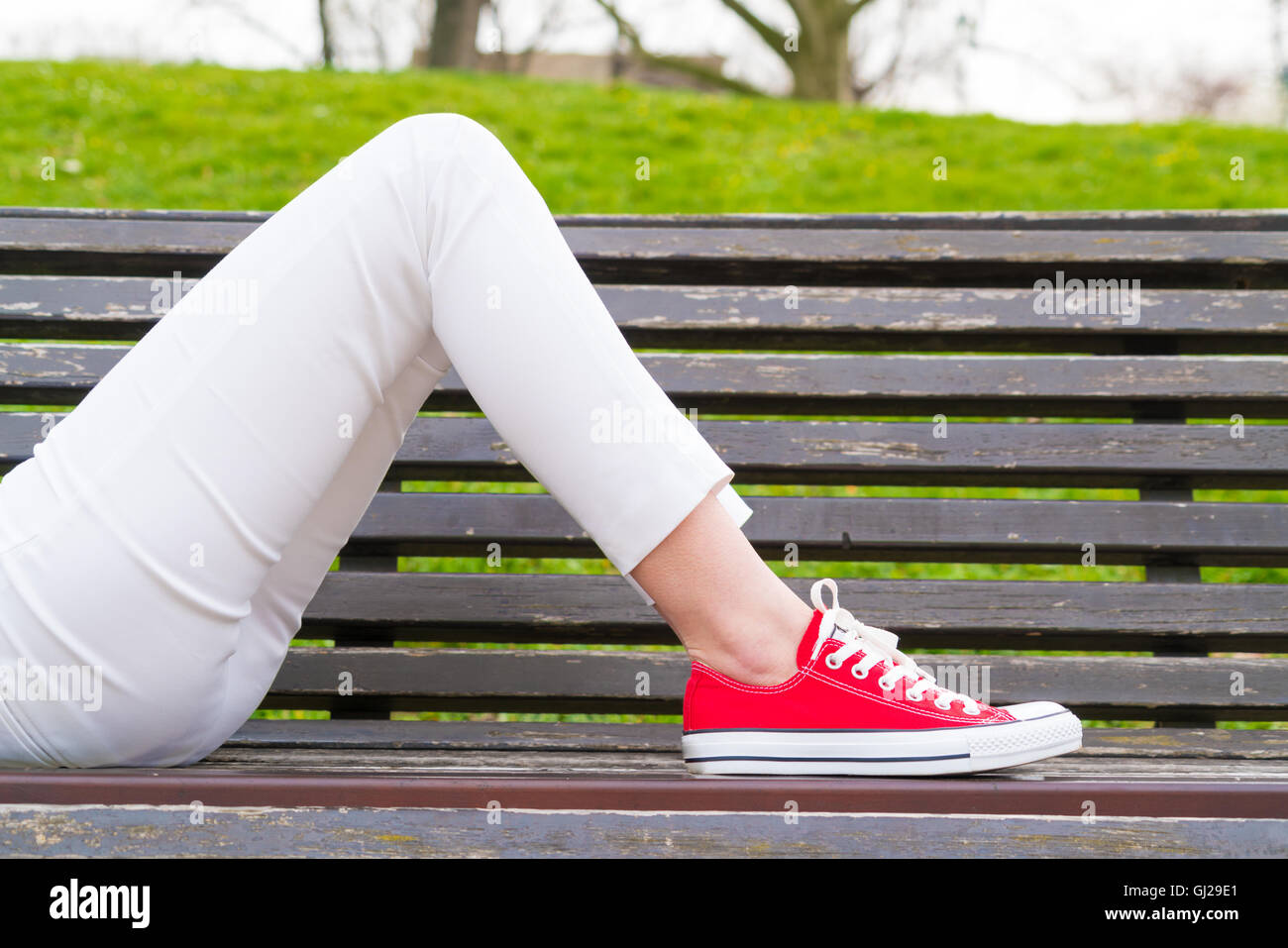 La ragazza giace su una panchina indossa sneakers Foto Stock
