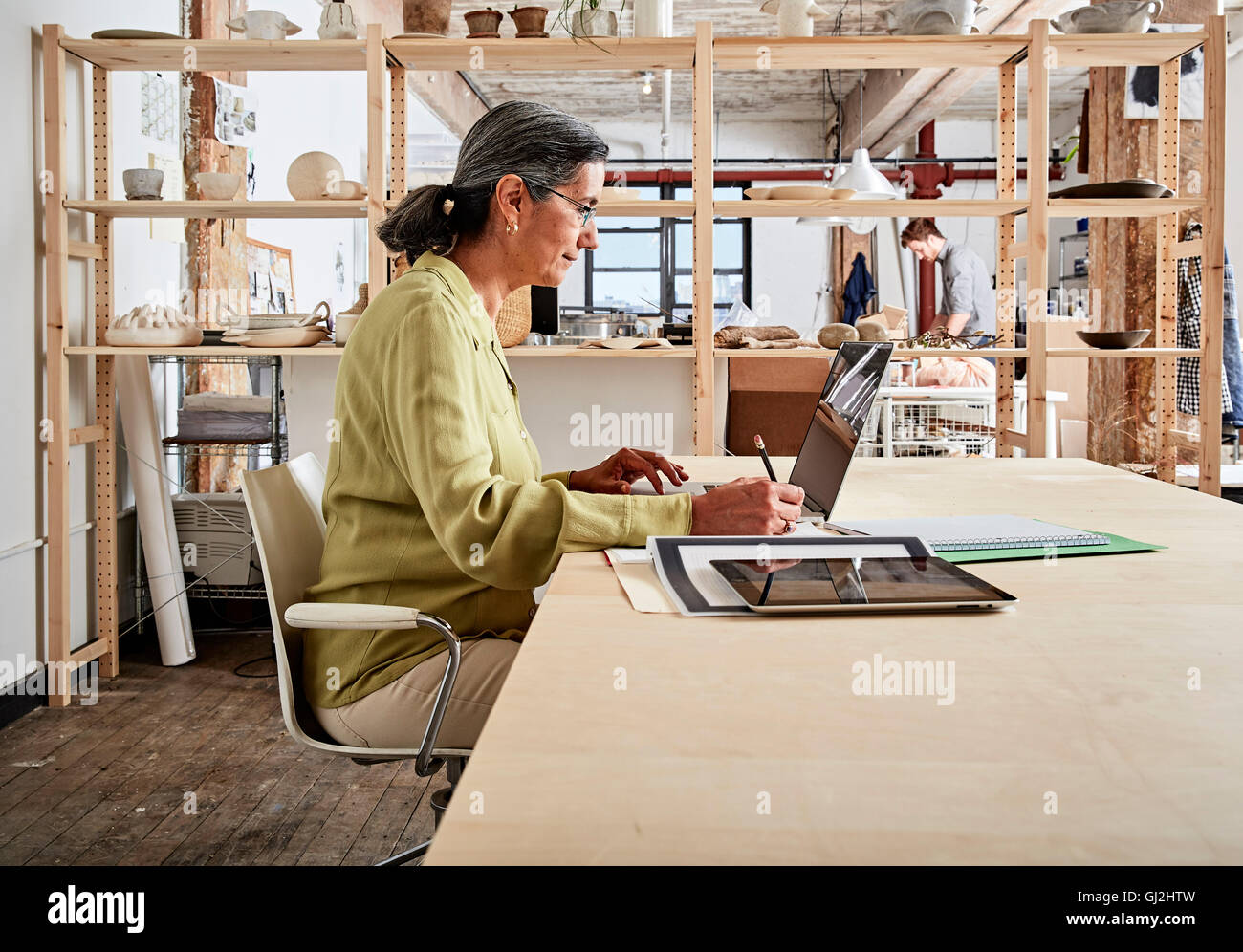 Vista laterale della donna alla scrivania in officina con laptop Foto Stock