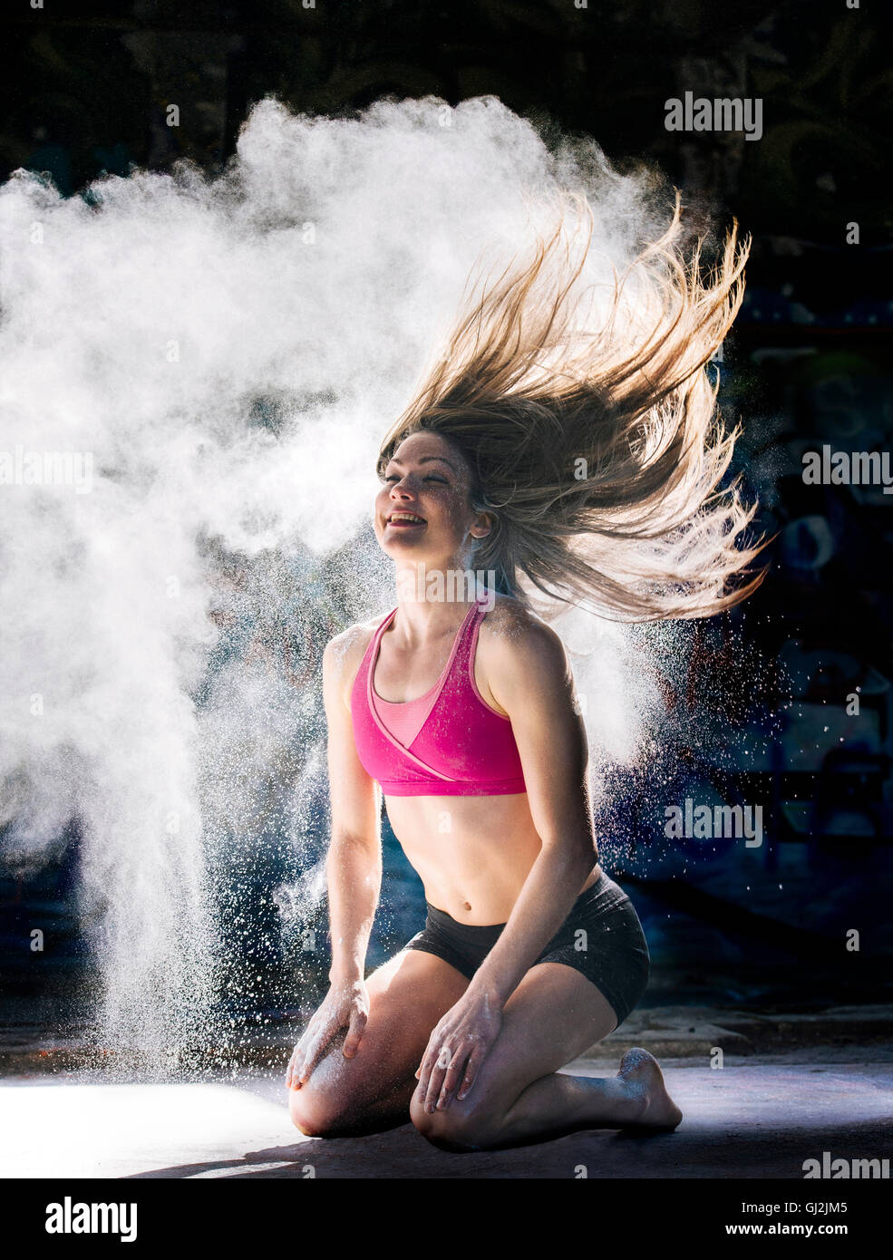 Donna inginocchiata gettare polvere oggetto capelli indietro sorridente Foto Stock