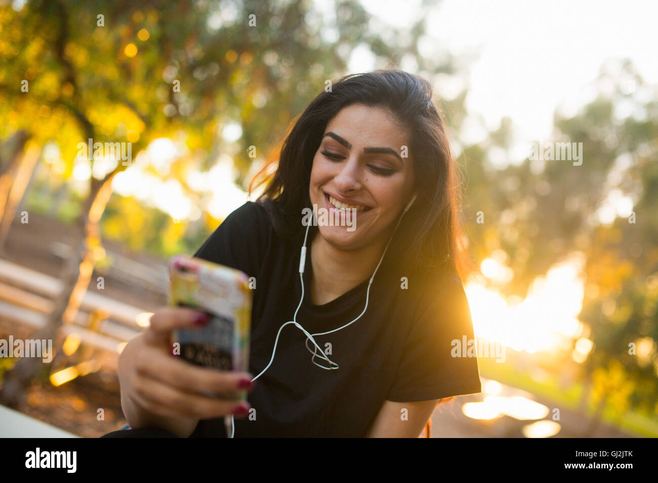 Giovane donna, all'aperto, indossa gli auricolari, tenendo lo smartphone Foto Stock
