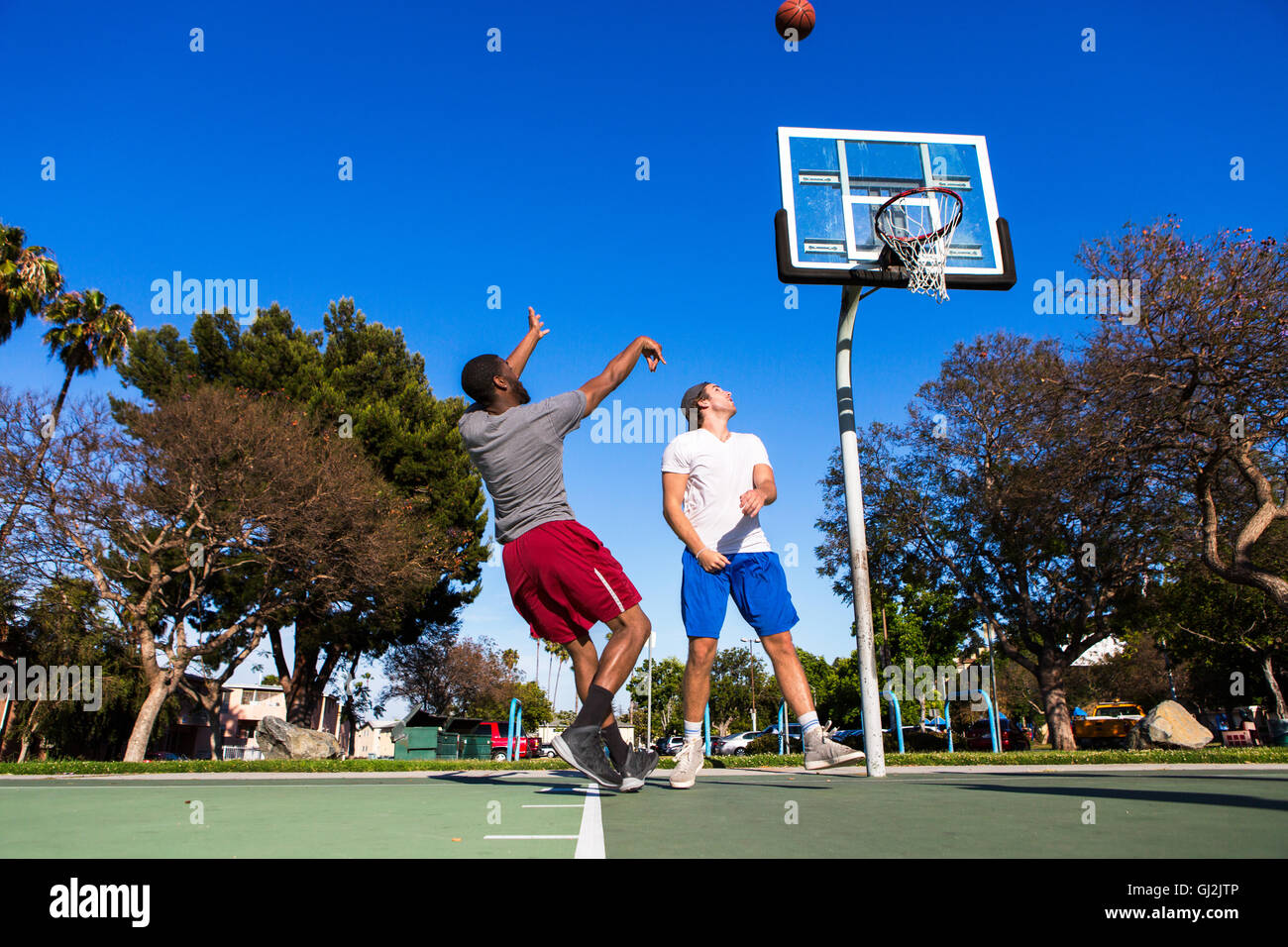 Giovane uomo gettando il basket verso il basket net sulla corte esterna Foto Stock