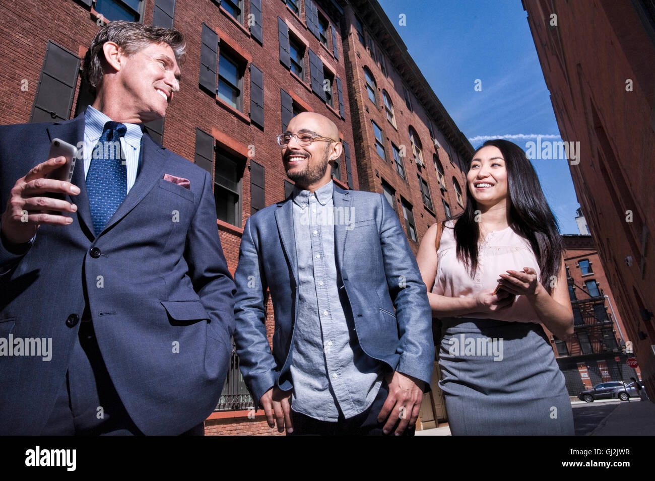 Business di uomini e donne a piedi all'aperto, tenendo lo smartphone, sorridente, basso angolo di visione Foto Stock