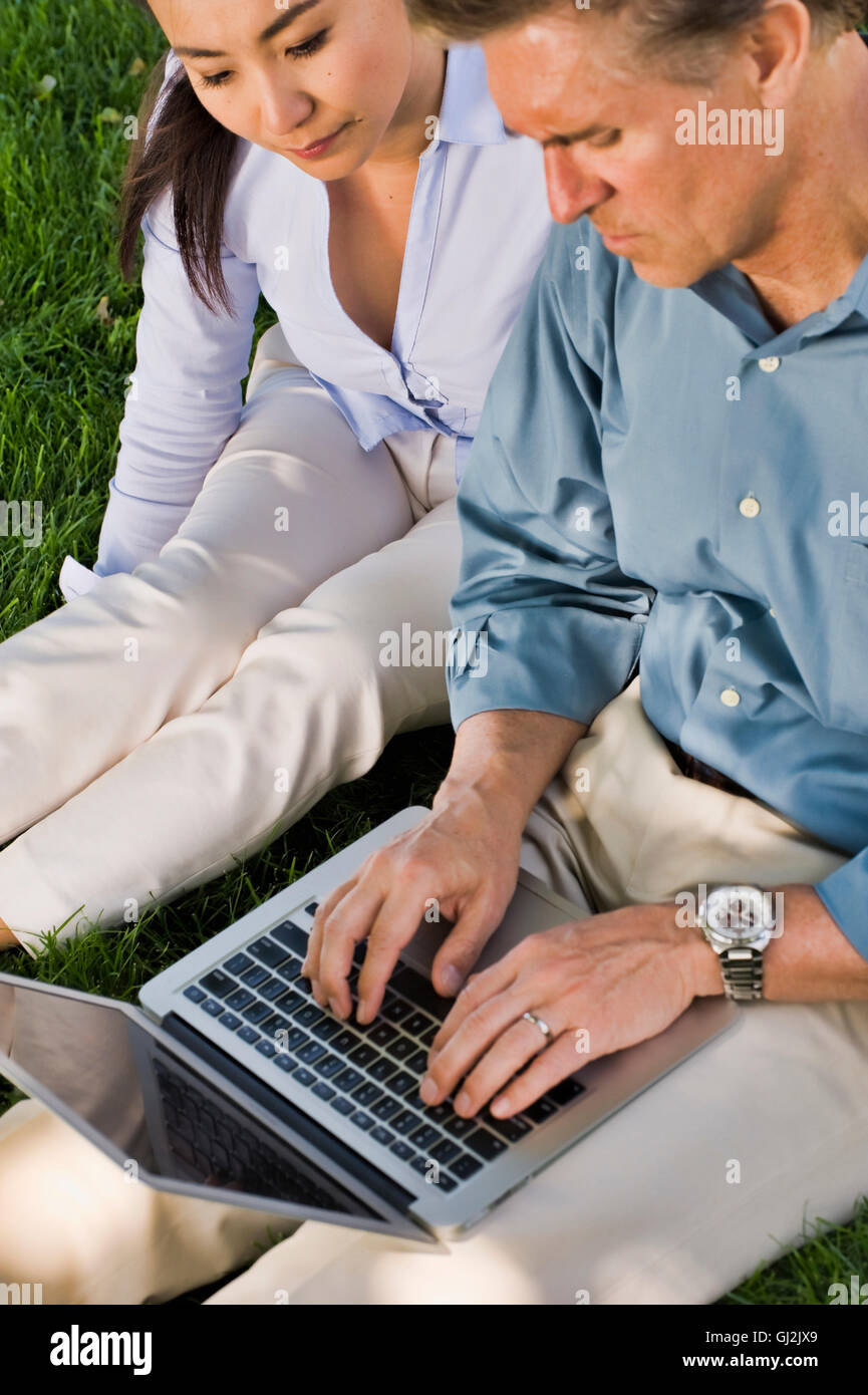 Business l uomo e la donna seduti all'aperto sull'erba, utilizzando laptop Foto Stock