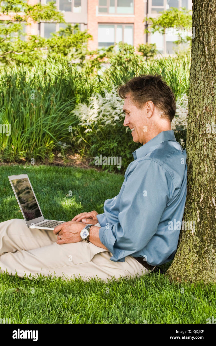 Imprenditore seduti all'aperto, appoggiata ad albero, utilizzando laptop Foto Stock