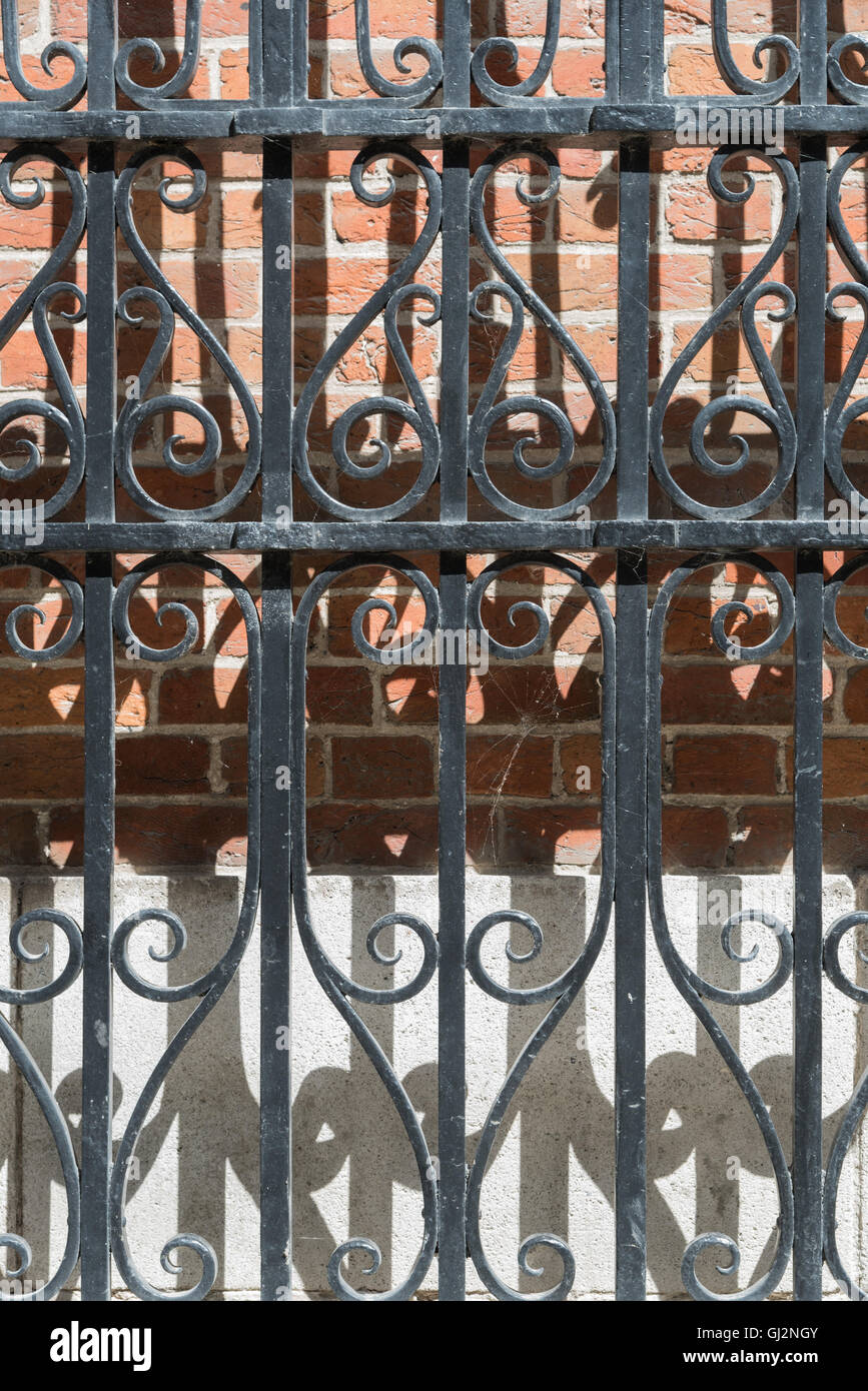 Un ornati in ferro battuto cancello anteriore. Curve e patterns ripetuti in ombre. Di mattoni rossi dietro. In Bruges. Foto Stock