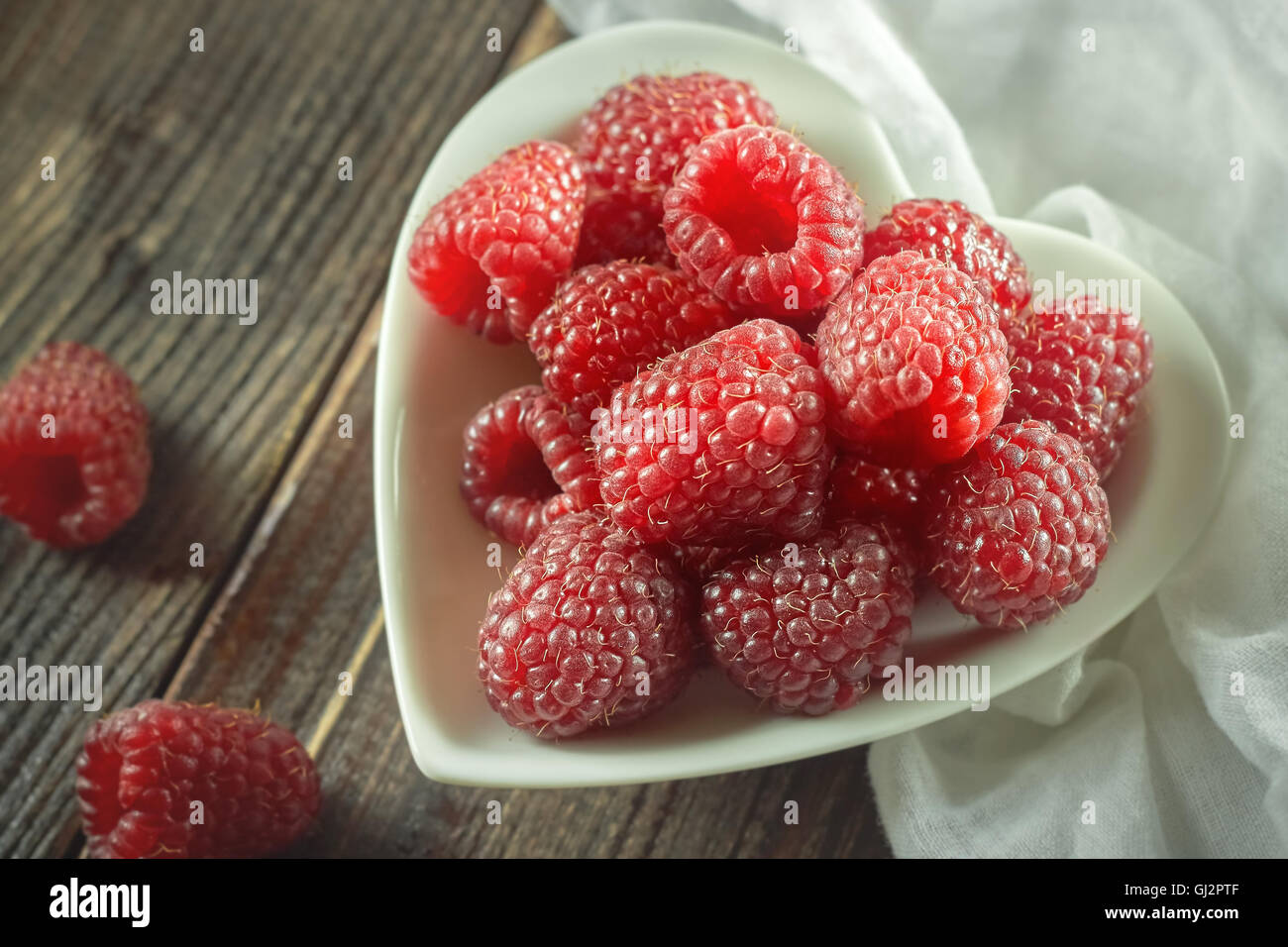 Il lampone rosso in ceramica bianca a forma di cuore sulla ciotola sfondo di legno Foto Stock