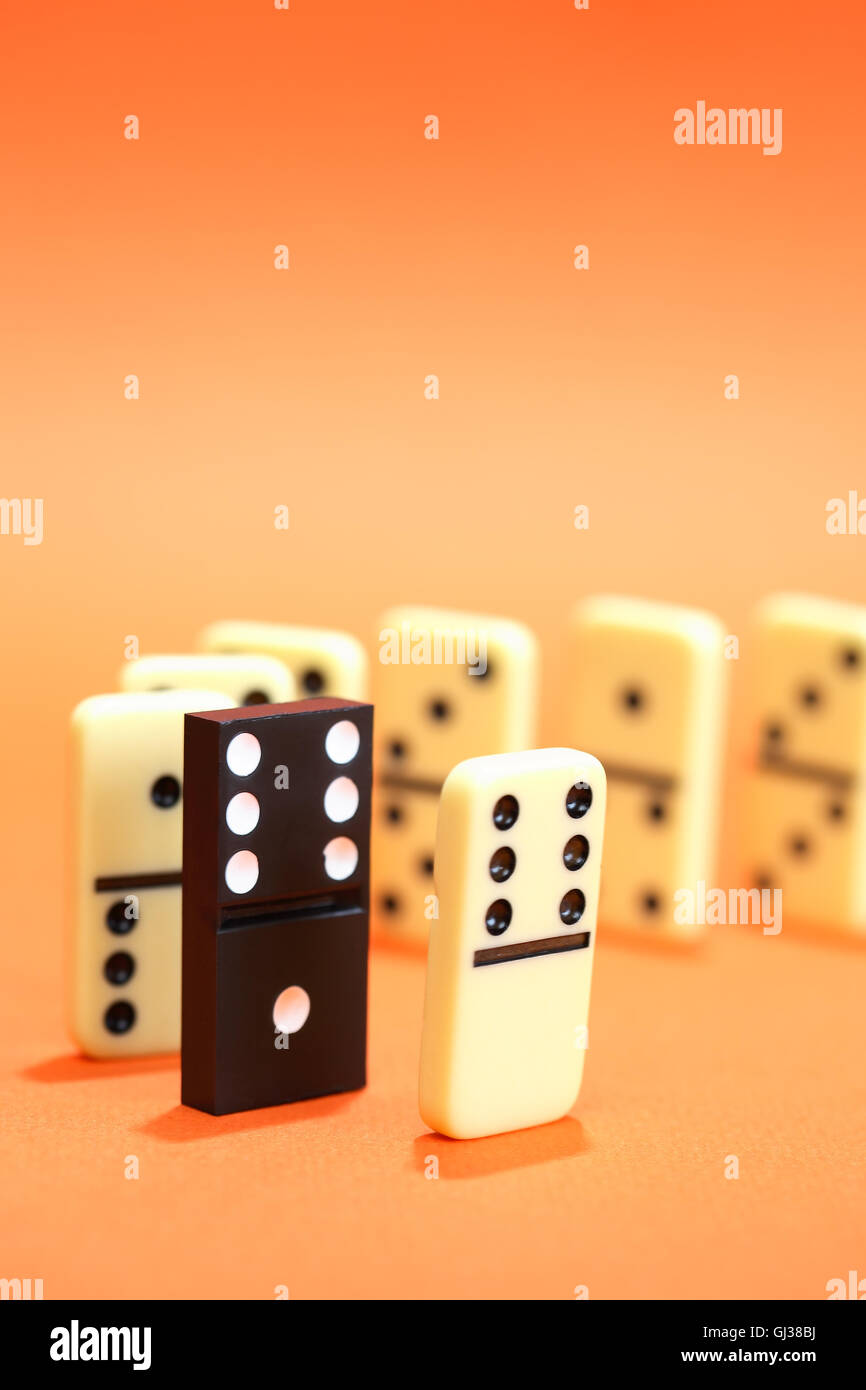 Domino nero tra white domino in piedi in fila su sfondo rosso Foto Stock