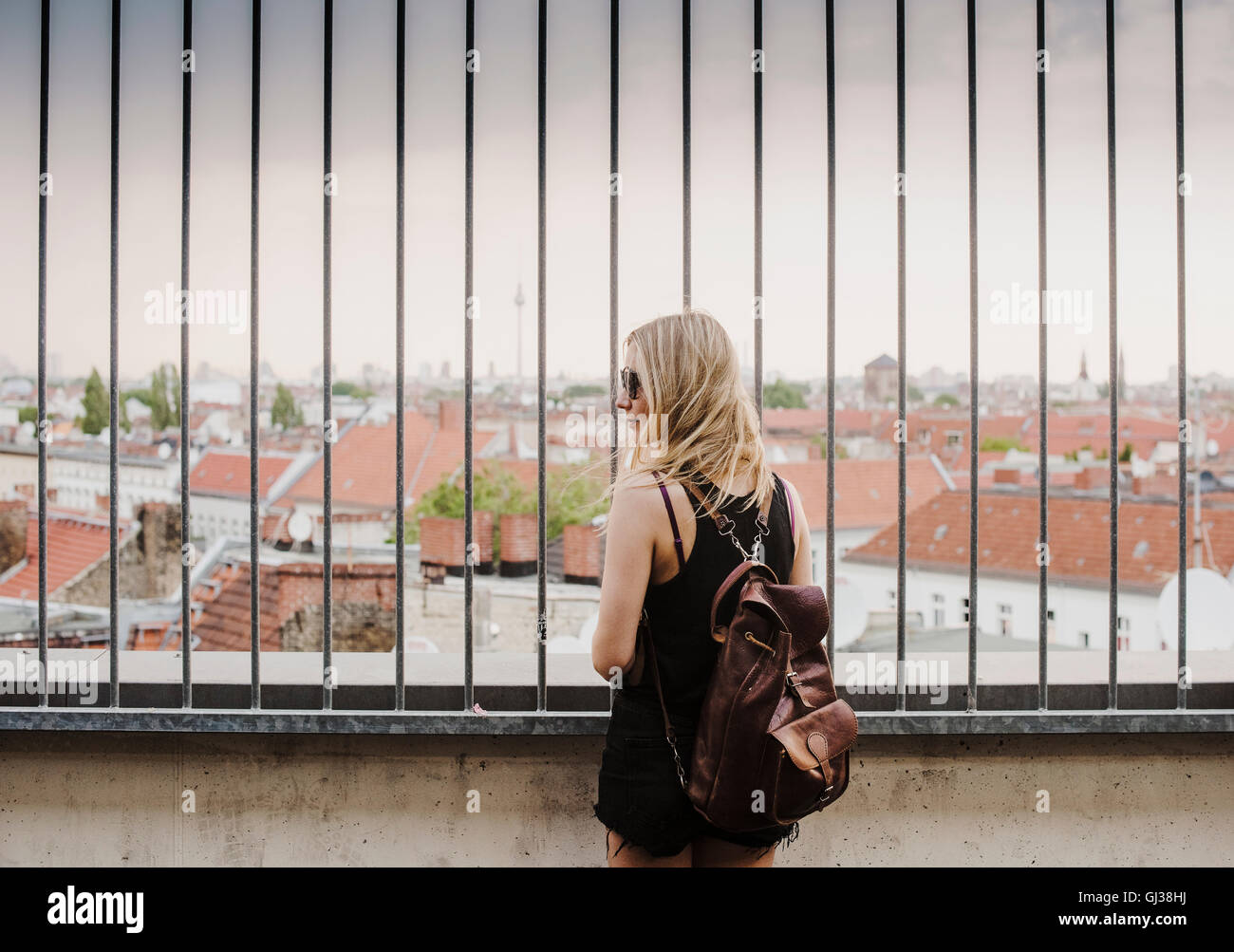 Giovane donna guardando attraverso le ringhiere, a vista sui tetti, vista posteriore Foto Stock