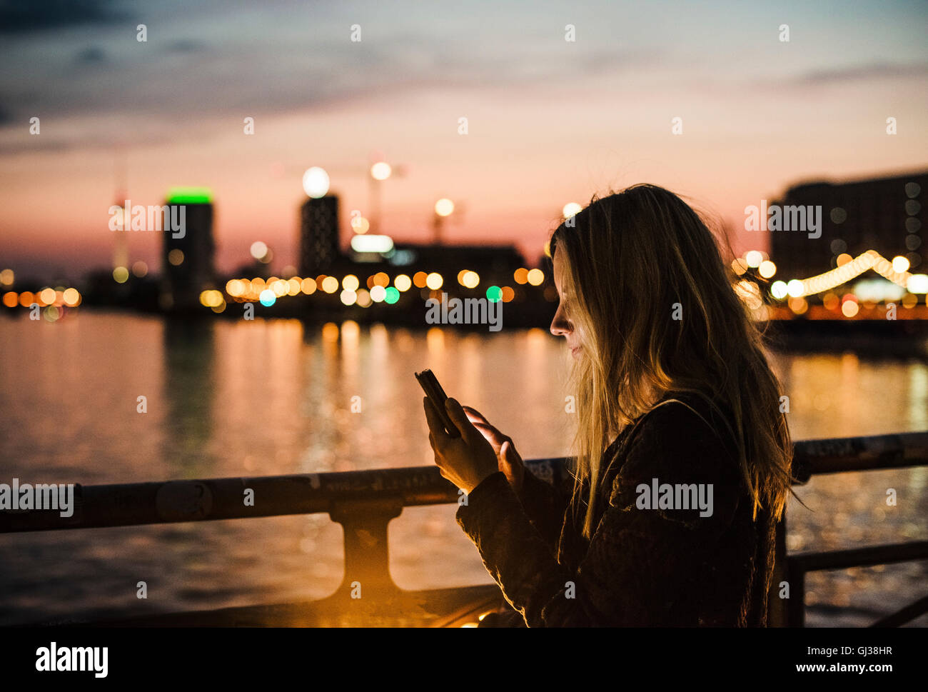 Giovane donna dal lungomare, al tramonto, utilizza lo smartphone Foto Stock