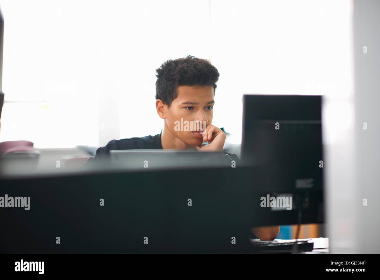 Maschio giovane studente di college alla scrivania del computer di lettura Foto Stock