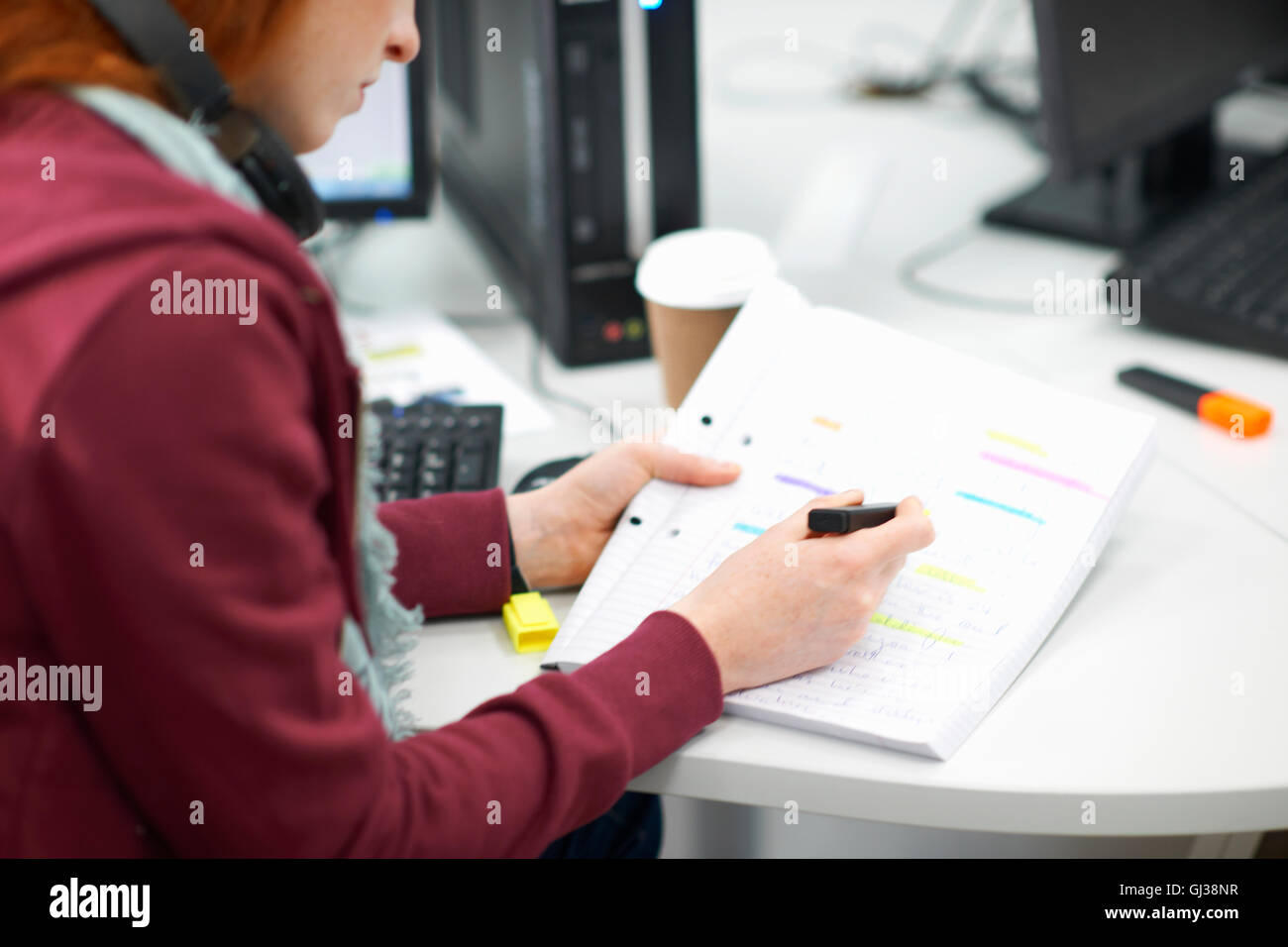 Femmina giovane studente di college a computer desk scrivendo in notebook Foto Stock