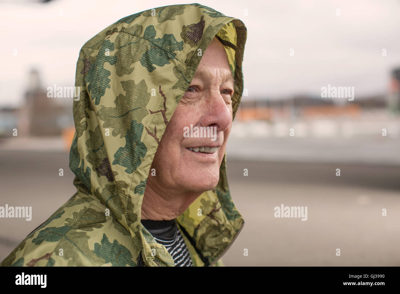 Uomo che indossa il camuffamento impermeabile cappotto con cappuccio che guarda lontano Foto Stock