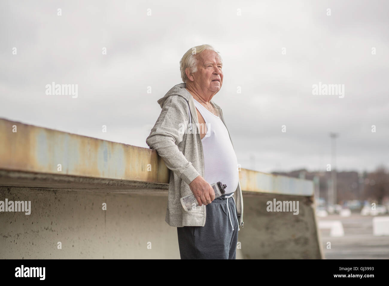 Uomo di indossare abbigliamento sportivo tenendo la bottiglia di acqua che guarda lontano Foto Stock